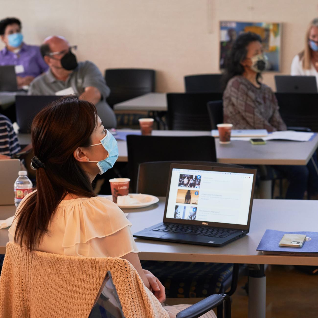 Image of attendees at tables, listening to a talk