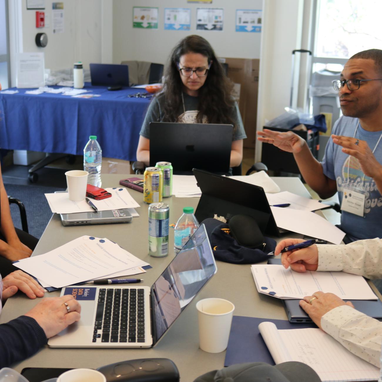 California educators seated around a table covered in laptops and notepads listen as one person talks enthusiastically
