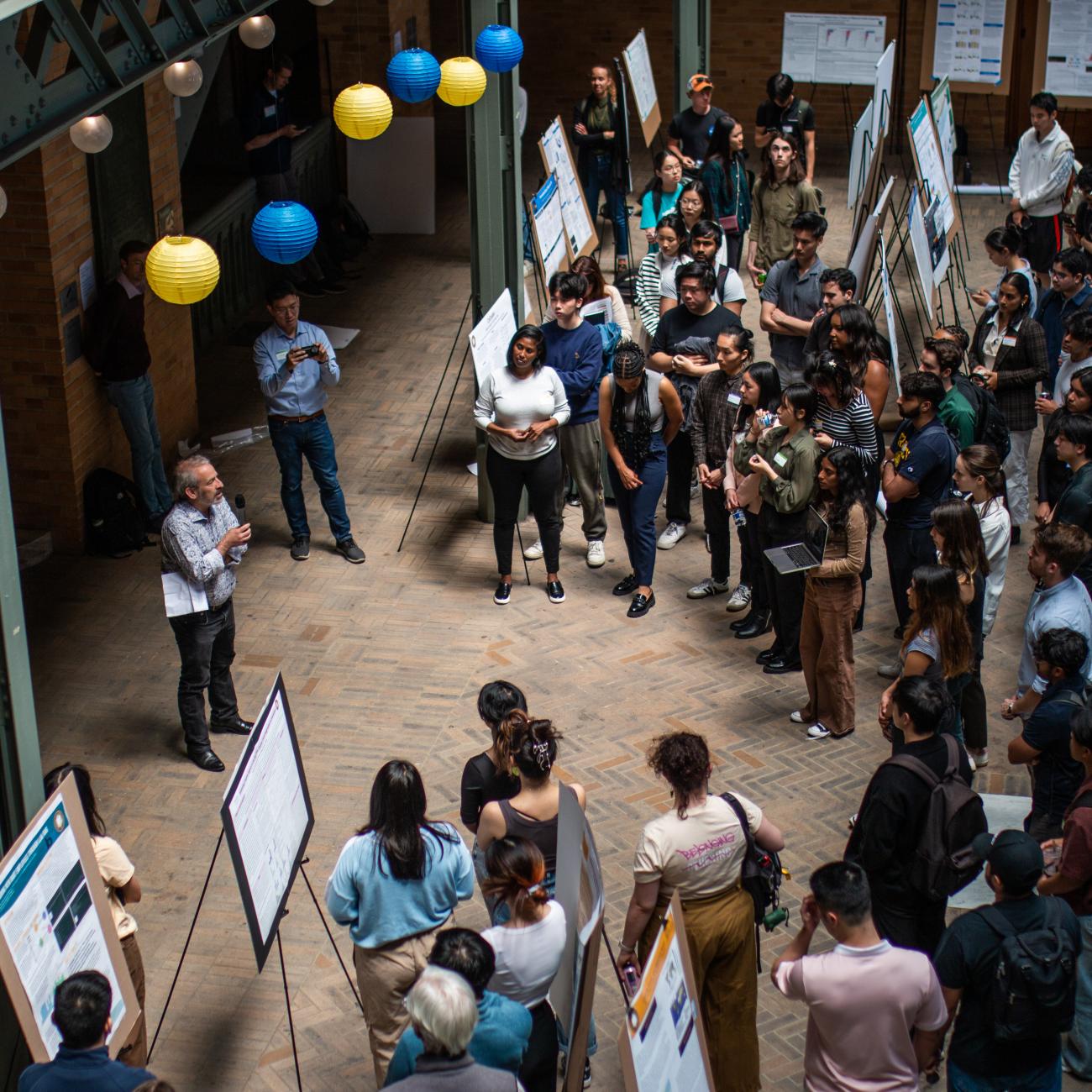 Amid poster board displays, crowd of students and guests listen to speaker at Spring 2024 Discovery Symposium 