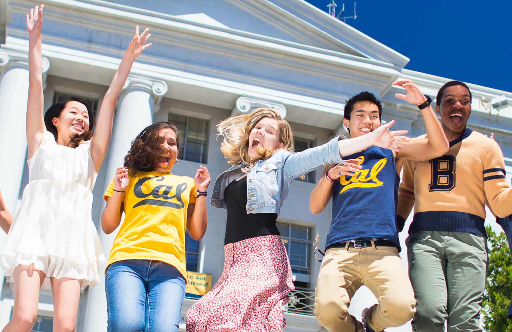 group of students jumping in the air and smiling in front of white building