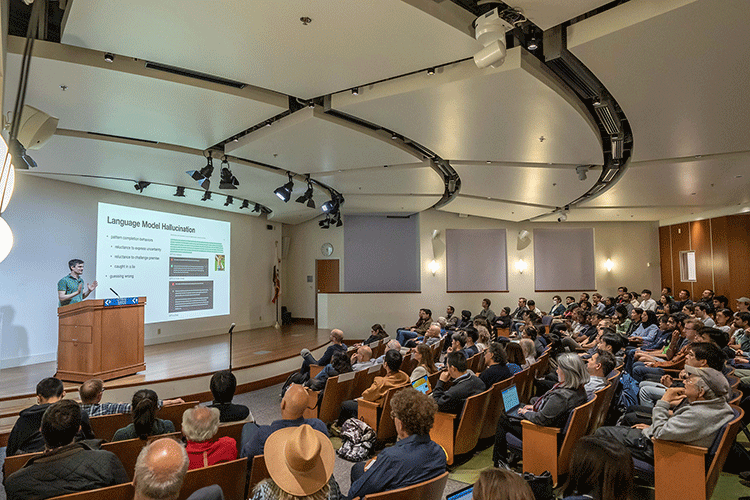 A photo of John Schulman at a podium, speaking to a full auditorium