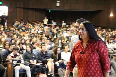 Ani Adhikari walks offstage in front of a crowded auditorium of students