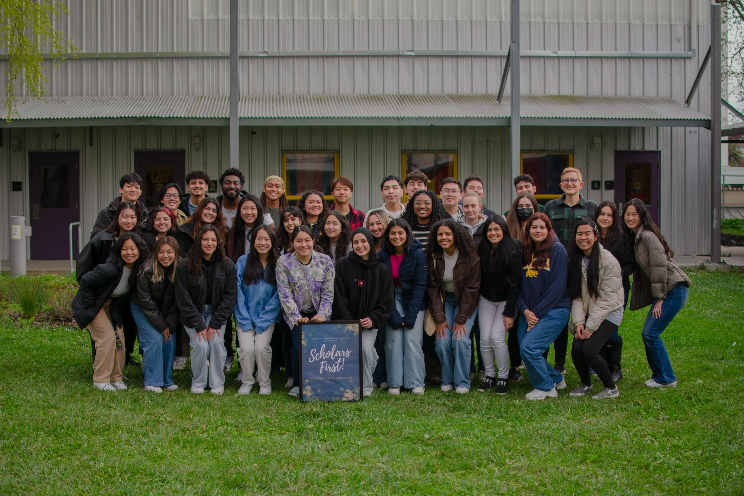 Data Scolars students pose on a lawn in front of a Scholars First sign.