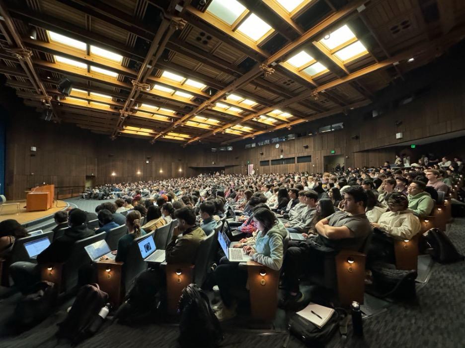 A lecture hall is filled with students with laptops open to take notes