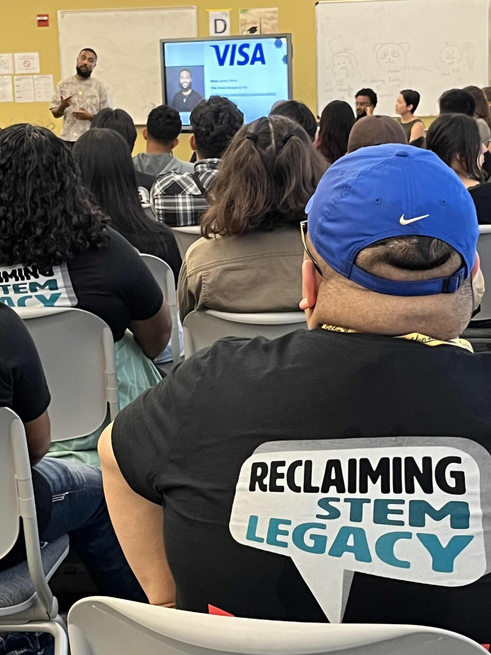 Puente Students listen to a data science career professional, wearing shirts emblazoned with, "Reclaiming STEM Legacy" 