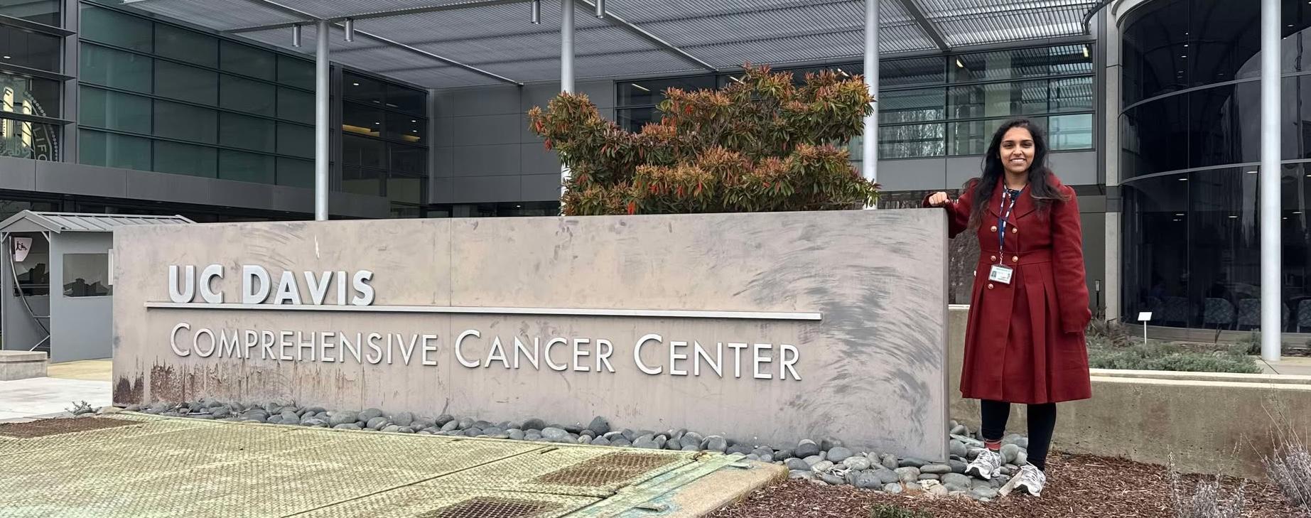 Jhinuk Barman, B.A. '19, stands with UC Davis Cancer Center sign out front of building