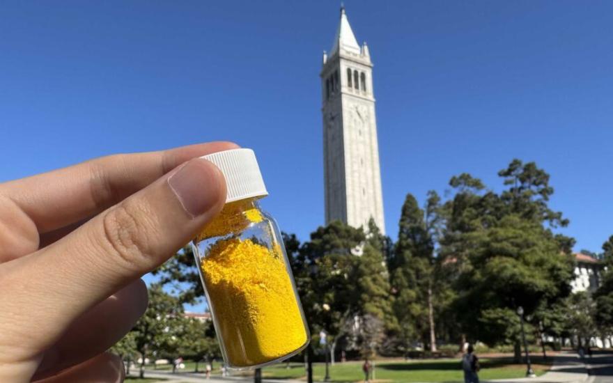 A vial of COF-999, which is yellow, with UC Berkeley’s landmark campanile in the background.